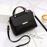 Cartera estructurada de cuero sintético negro, con solapa frontal y detalle metálico dorado. Cuenta con asa rígida superior y correa ajustable y desmontable para usar cruzada o al hombro.