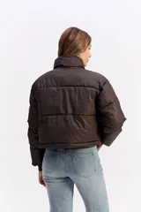 Campera puffer de corte cropped, color marrón oscuro, con cuello alto, cierre frontal con cremallera y botones a presión, y puños elásticos.