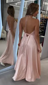 Vestido largo de satén color rosado, con diseño cruzado, escote en V pronunciado, tirantes finos tipo halter y lazo ajustable en la cintura.