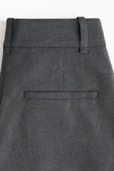 Pantalón sastrero gris oscuro de corte holgado con tiro alto, cierre con corchete y botón ocultos. Presenta piernas amplias con pinzas, raya marcada en el frente y la parte trasera, bolsillos al bies y bolsillos decorativos en la parte posterior.
