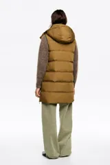 Chaleco acolchado de largo medio y corte en línea A, confeccionado en tejido técnico color beige con detalles en negro. Presenta cuello subido, capucha desmontable, cierre frontal de cremallera, bolsillos laterales con cremallera, logo bordado en el pecho y aberturas laterales con cremallera.