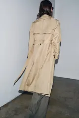 Trench color beige con cuello solapa y manga larga ajustable con trabillas. Bolsillos en delantero. Cinturón en mismo tejido. Detalle de pespuntes marcados a tono. Cierre frontal cruzado con botones. Tejido repelente al agua.