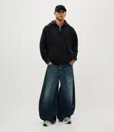 Pantalón de jean con calce barrel, caracterizado por su volumen amplio en las piernas y un sutil ajuste en la botamanga. Presenta costuras desplazadas y un lavado medio, confeccionado en algodón resistente.