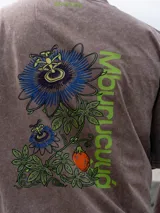 Remera Brixton oversize de algodón, color marrón con efecto acid wash, manga corta y estampa en la espalda de flores de mburucuyá con el texto vertical en color verde.