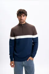 Buzo de tejido de punto con diseño de bloques de color en tonos marrón, blanco y azul marino. Presenta cuello alto con medio cierre frontal, mangas largas y puños y ruedo acanalados.