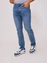 Jean de corte slim fit con cintura media y cierre frontal con botón y cremallera. Presenta un lavado azul clásico con costuras en contraste.