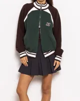 Campera de punto de algodón de grosor medio, con cierre frontal, cuello alto y puños y cintura en rib con franjas blancas y marrones. El cuerpo es verde oscuro y las mangas son marrones. Lleva un parche bordado con doble logo en el pecho.