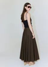 Falda larga color marrón oscuro, con diseño evasé, tiro medio y detalle cruzado tipo pañuelo con cierre de nudo en la cintura.