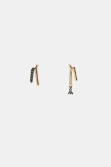 Pendientes asimétricos de metal dorado. Un pendiente presenta dos barras verticales, una de ellas incrustada con pequeñas piedras oscuras. El otro pendiente presenta dos barras verticales con un dije colgante de forma geométrica con piedras oscuras en la parte inferior.
