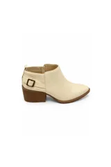 Bota corta de color marfil con punta afinada, taco medio de madera y detalle de hebilla metálica lateral. Cuenta con un diseño que combina acabado liso en la parte delantera y textura estriada en la parte trasera.