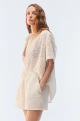 Camisa amplia y relajada de algodón liviano color blanco, de trama abierta y textura, con cuello camisero, mangas cortas y cierre de botones al frente.