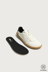 Zapatillas deportivas barefoot de hombre elaboradas en piel. Diseño en color blanco con detalles en negro y beige en el talón, y suela plana de goma marrón.