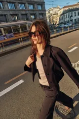 Chaqueta corta de color marrón oscuro, con cuello de solapa, manga larga con trabillas en los puños, bolsillos delanteros con solapa y cierre frontal con botones.