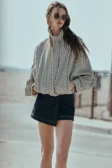 Chaqueta estilo bomber con estampado de cuadros vichy en blanco y negro, de cuello subido, manga larga y bolsillos delanteros de vivo. Cuenta con bajo abullonado y cierre frontal con cremallera oculta.