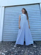 Mono largo de corte holgado con diseño de rayas verticales finas en azul y blanco. Presenta breteles anchos para atar sobre los hombros y piernas de corte ancho tipo palazzo.