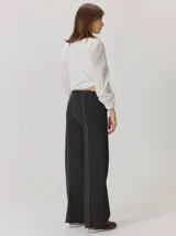 Pantalón de corte relajado color marrón, confeccionado en una mezcla de algodón y elastano. Presenta costuras en contraste color rojo en bolsillos y bragueta, con cierre de botón metálico.