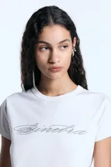 Remera de jersey de algodón con calce ajustado, escote redondo y manga corta. Presenta una estampa frontal con diseño de letras en glitter.