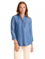 Blusa de lyocell color azul con efecto denim, cuello camisero con solapa y escote en V con cierre de un botón. Presenta mangas tres cuartos con terminación doblada y ruedo redondeado.