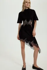 Vestido midi de terciopelo negro con cuello redondo y pañuelo integrado en el mismo tejido. Presenta mangas cortas, aberturas laterales con detalle de encaje a tono y bajo asimétrico con terminación en encaje.