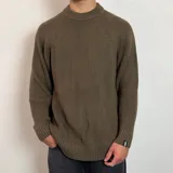 Sweater de tejido de punto grueso en color beige, con cuello redondo y mangas raglán. Presenta un diseño holgado y una pequeña etiqueta con logo en el puño.
