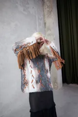 Sweater tejido a mano con diseño de ochos, con apliques de tiras de cuero entrelazadas y flecos en las mangas. Presenta un estampado artístico pintado a mano con efecto degradado en tonos blanco, gris y marrón.