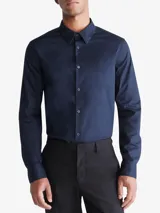 Camisa de vestir azul marino de manga larga, con cuello clásico y cierre con botones. Presenta un logo bordado en el pecho. Corte entallado.