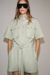 Mono corto de Zara Woman Collection color verde menta, confeccionado en mezcla de algodón y lino. Presenta cuello solapa, manga corta, cierre frontal con botones, bolsillos de plastrón con solapa en el pecho y cintura ajustable con lazo.