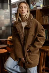 Campera tipo gamulán de efecto gamuza color marrón, con interior de corderito sintético. Presenta cierre frontal, bolsillos delanteros con solapa y cintura ajustable con cordón.