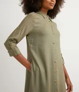 Vestido chemise largo color naranja, confeccionado en viscolino. Tiene cuello solapa, cierre con botones, manga larga con martingale, aberturas laterales y no tiene estampado.