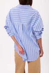 Camisa de corte oversize con diseño de rayas verticales en tonos celeste y blanco, cuello clásico y cierre frontal con botones.