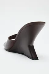 Zapato tipo mule de piel color marrón, con tacón de cuña asimétrica de madera y acabado en punta redonda.