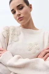 Sweater de punto en color beige melange, con cuello redondo y mangas largas. Presenta apliques de flores tejidas en relieve sobre los hombros y el pecho.