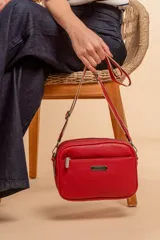 Bandolera de diseño rectangular con textura granulada, color verde oliva. Cuenta con tres compartimentos principales con cierre, un bolsillo frontal adicional y correa ancha ajustable de tela en tono a juego.