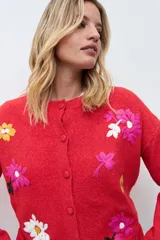 Cardigan de punto color rojo con cierre frontal de botones y bordados de flores en diversos colores. Presenta cuello redondo y mangas largas con puños acanalados.