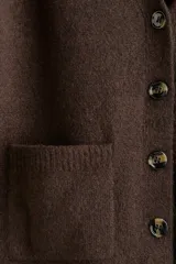 Cárdigan de punto suave color marrón oscuro, con cuello en V, botones frontales y bolsillos abiertos en la parte delantera. Presenta hombros caídos y remates acanalados en puños y bajo.