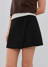 Minifalda negra de tiro medio, con diseño cruzado tipo envolvente (wrap) en el frente.