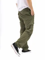 Pantalón de trekking convertible color verde militar, con piernas removibles mediante cierre a la altura de la rodilla, transformándolo en bermuda. Presenta múltiples bolsillos cargo con tapa y cierre, y cintura con pasadores para cinturón.