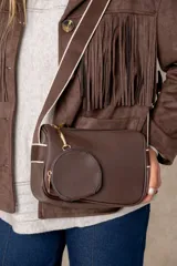 Cartera bandolera color chocolate con textura granulada, que incluye un monedero circular desmontable sujeto a la correa. Posee cierre superior y correa ajustable con detalles en color crema.