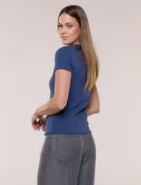 Remera básica de corte al cuerpo con textura acanalada, cuello redondo y mangas cortas. Presenta una pequeña placa metálica decorativa en el borde inferior.