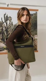 Cartera tipo hobo de tamaño grande en color beige, con detalles en negro. Presenta una franja horizontal negra con el logo de la marca, asa corta de hombro y correa larga desmontable. Incluye bolsillo frontal con cierre oculto y bolsillo trasero.