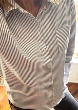 Camisa de popelina a rayas verticales blancas y azules, de estilo clásico con cuello, bolsillo frontal con rayas en dirección horizontal, cierre delantero con botones de nácar y mangas largas con puños.