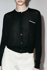Chaqueta de punto de efecto doble capa color negro, con cuello redondo y ribete blanco, manga larga y cierre frontal con botones. Cuenta con un bolsillo de parche en el pecho con detalle en contraste.