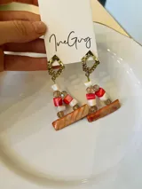 Aros colgantes con base dorada y dijes de nácar en forma de rectángulo, cuentas rojas, blancas y transparentes.