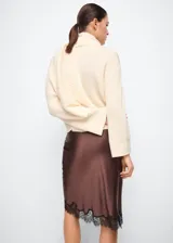 Jersey de punto color marfil con cuello alto y bufanda integrada del mismo tejido y textura acanalada, de diseño holgado y manga larga.