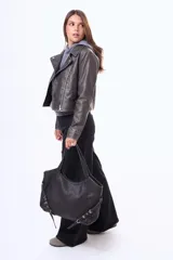 Cartera tipo bolso de hombro color negro, confeccionada en material simil cuero. Presenta un diseño amplio con cierre superior, asas fijas y detalles de correas decorativas con hebillas metálicas en los laterales.