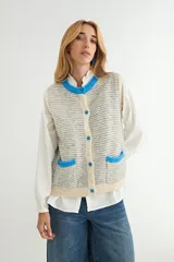 Chaleco de punto con diseño a rayas horizontales en gris y blanco. Presenta cuello redondo, bordes y bolsillos frontales con detalles en color rojo, y cierre frontal con botones rojos.