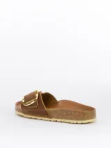 Sandalias tipo slide modelo Madrid Big Buckle de Birkenstock, color cognac. Presentan una correa ancha de cuero nubuck engrasado con una hebilla metálica dorada de gran tamaño. Cuentan con una plantilla anatómica de corcho y látex forrada en cuero napa y suela de EVA.