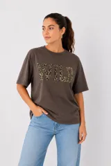 Remera de algodón color marrón oscuro, de corte holgado y manga corta, con cuello redondo a la base y estampa frontal con la palabra WILD en animal print.