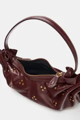 Bolso de hombro de diseño fruncido con cordones ajustables en los laterales y tachas metálicas doradas distribuidas por toda la superficie. Cuenta con asa corta de hombro y cierre superior con cremallera.