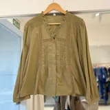 Camisa verde militar de manga larga con detalles de encaje y bordados en los hombros, cuello en V con volados y cierre frontal con botones.